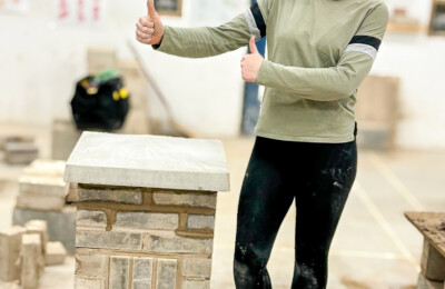 female adult student posing with a thumbs up next to the brickwork project she has completed during the free adult course.